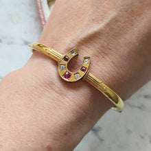 Load image into Gallery viewer, A yellow gold horseshoe bangle bracelet with rubies and diamonds, modelled on a wrist