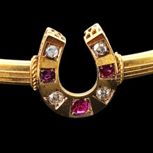 Load image into Gallery viewer, Close-up of a yellow gold horseshoe bangle bracelet with rubies and diamonds, on a black background