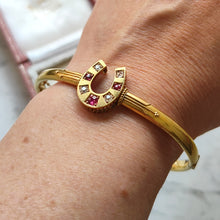 Load image into Gallery viewer, A yellow gold horseshoe bangle bracelet with rubies and diamonds, modelled on a wrist