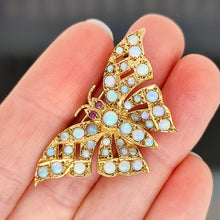 Load image into Gallery viewer, A yellow gold butterfly brooch with opals and ruby eyes, held in a hand