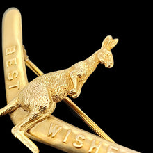 Load image into Gallery viewer, A boomerang shaped brooch with a kangaroo reading BEST WISHES, in yellow gold, on a black background