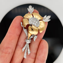 Load image into Gallery viewer, A two tone gold flower brooch with diamonds, held in a hand