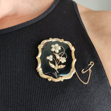 Load image into Gallery viewer, A black onyx, pearl and diamond flower brooch in yellow gold, modelled by a woman wearing a black top
