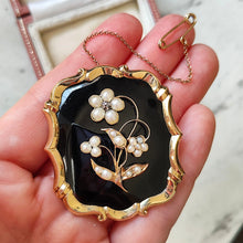 Load image into Gallery viewer, A black onyx, pearl and diamond flower brooch in yellow gold, held in a hand
