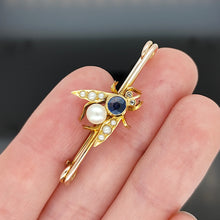 Load image into Gallery viewer, A yellow gold fly bar brooch with sapphire, pearls and diamond eyes, held in a hand