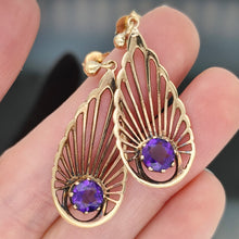 Load image into Gallery viewer, A pair of pear shaped fan design drop earrings with amethysts in yellow gold, held in a hand
