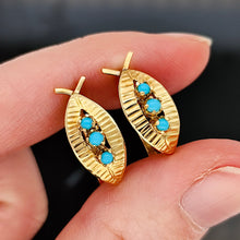 Load image into Gallery viewer, A pair of yellow gold turquoise leaf shaped earrings, held in a hand