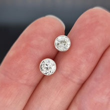 Load image into Gallery viewer, Diamond stud earrings held between two fingers against a neutral background