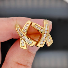 Load image into Gallery viewer, A pair of yellow gold round diamond cross shaped stud earrings, held between fingers