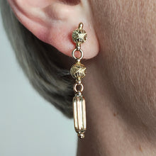 Load image into Gallery viewer, An engraved bead and bar drop earring in yellow gold, modelled in an ear