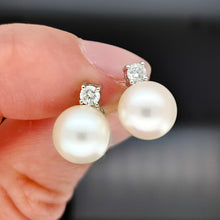 Load image into Gallery viewer, A pair of white pearl and round diamond stud earrings in white gold, held in a hand