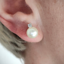 Load image into Gallery viewer, A white pearl and round diamond stud earrings in white gold, modelled in an ear