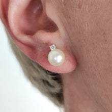 Load image into Gallery viewer, A white pearl and round diamond stud earrings in white gold, modelled in an ear