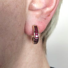 Load image into Gallery viewer, A yellow gold hoop earring channel set with square cut rubies, modelled in an ear