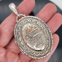 Load image into Gallery viewer, Decorative silver pendant held in a hand with a blurred background