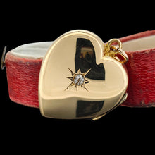 Load image into Gallery viewer, A yellow gold heart shaped locket with a diamond, leaning against a red box