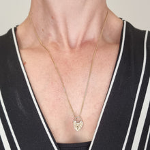 Load image into Gallery viewer, Gold necklace with a heart-shaped pendant worn by a person in a black and white striped garment.