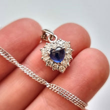 Load image into Gallery viewer, A heart shaped sapphire and diamond cluster pendant, with a curb link chain, held in a hand