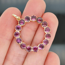 Load image into Gallery viewer, A circular yellow gold pendant with almandine garnets, held in a hand