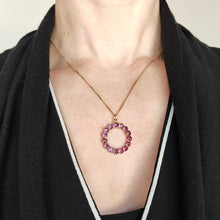 Load image into Gallery viewer, A circular yellow gold pendant with almandine garnets, modelled with a gold chain by a woman wearing a black and white dress
