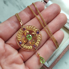 Load image into Gallery viewer, A peridot and amethyst yellow gold drop pendant, with a chain, held in a hand