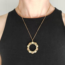 Load image into Gallery viewer, A yellow gold ruby and pearl flower open circle pendant, with a chain, modelled by a woman wearing a black top