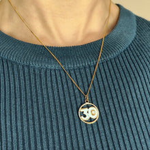 Load image into Gallery viewer, A yellow gold 30 pendant with a brilliant cut diamond, modelled with a chain by a woman wearing a blue top