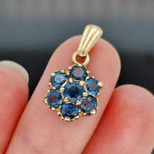 Load image into Gallery viewer, A yellow gold pendant with seven round sapphires, held on a fingertip, on a black background