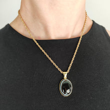 Load image into Gallery viewer, An oval banded agate pendant rubover set in yellow gold, with a yellow gold chain, modelled by a woman wearing a black top
