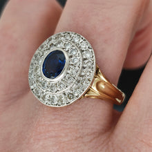 Load image into Gallery viewer, An oval sapphire and diamond cluster ring in yellow and white gold, modelled on a hand