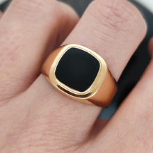 Load image into Gallery viewer, A cushion shaped onyx signet ring in yellow gold, modelled on a hand