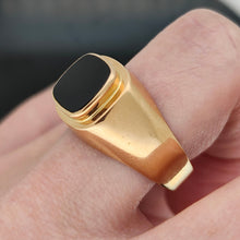 Load image into Gallery viewer, A cushion shaped onyx signet ring in yellow gold, modelled on a hand