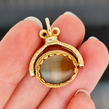Load image into Gallery viewer, An oval spinner fob pendant in yellow gold with agate, held in a hand