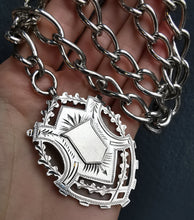 Load image into Gallery viewer, A silver Albert watch chain with large oval links, two lobster clasps, a T-bar and a shield shaped fob medal, held in a hand