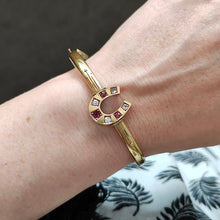 Load image into Gallery viewer, A yellow gold horseshoe bangle bracelet with rubies and diamonds, modelled on a wrist
