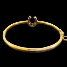 Load image into Gallery viewer, A yellow gold horseshoe bangle bracelet with rubies and diamonds, on a black background
