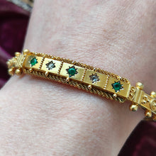 Load image into Gallery viewer, A yellow gold Etruscan style bangle bracelet set with emeralds and diamonds, modelled on a wrist
