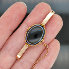 Load image into Gallery viewer, A bar brooch in yellow gold with an oval cabochon banded agate centre, held in a hand

