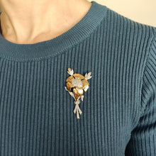 Load image into Gallery viewer, A two tone gold flower brooch with diamonds, modelled by a woman wearing a blue top
