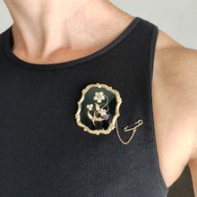 Load image into Gallery viewer, A black onyx, pearl and diamond flower brooch in yellow gold, modelled by a woman wearing a black top
