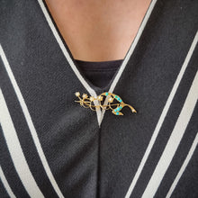 Load image into Gallery viewer, Gold brooch with turquoise stones modelled on a black and white striped garment

