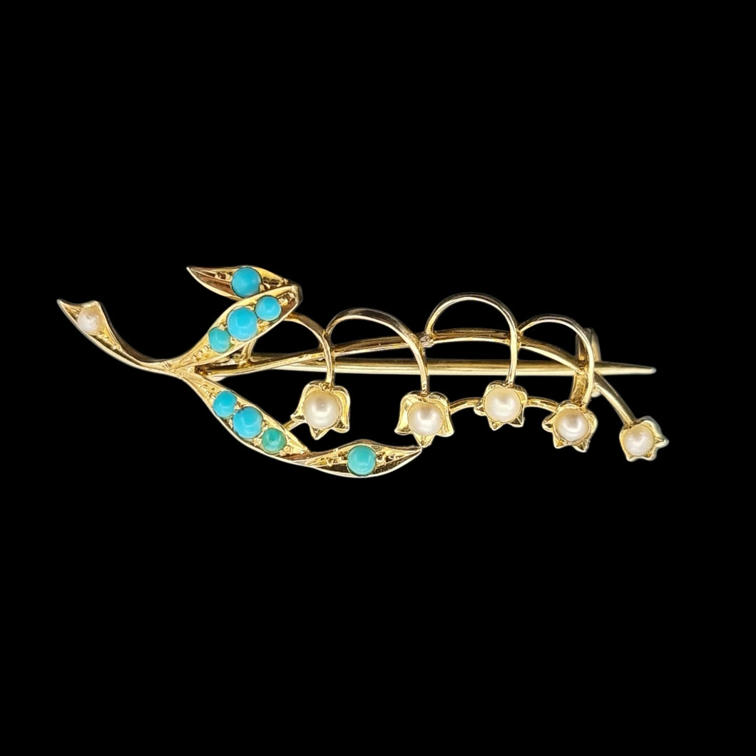 Gold floral brooch with turquoise stones and pearl-like elements on a black background
