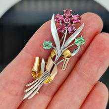Load image into Gallery viewer, A ruby and green zircon flower bouquet brooch in white and rose gold, held in a hand
