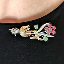 Load image into Gallery viewer, A ruby and green zircon flower bouquet brooch in white and rose gold, modelled by a woman wearing a black top
