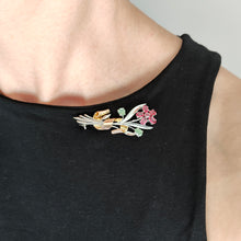 Load image into Gallery viewer, A ruby and green zircon flower bouquet brooch in white and rose gold, modelled by a woman wearing a black top
