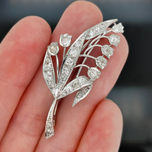 Load image into Gallery viewer, A white gold lily of the valley floral brooch set with diamonds, held in a hand
