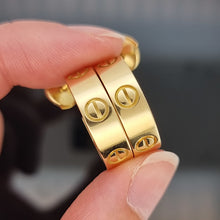 Load image into Gallery viewer, Gold Cartier hoop earrings held between fingers against a dark background
