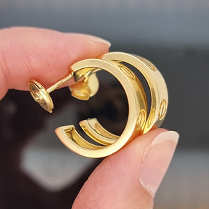 Gold Cartier hoop earrings held between fingers against a blurred background
