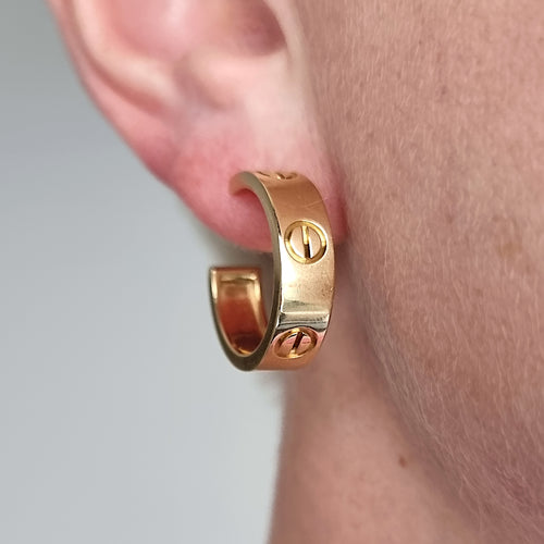Gold Cartier hoop earring worn on an ear with a neutral background