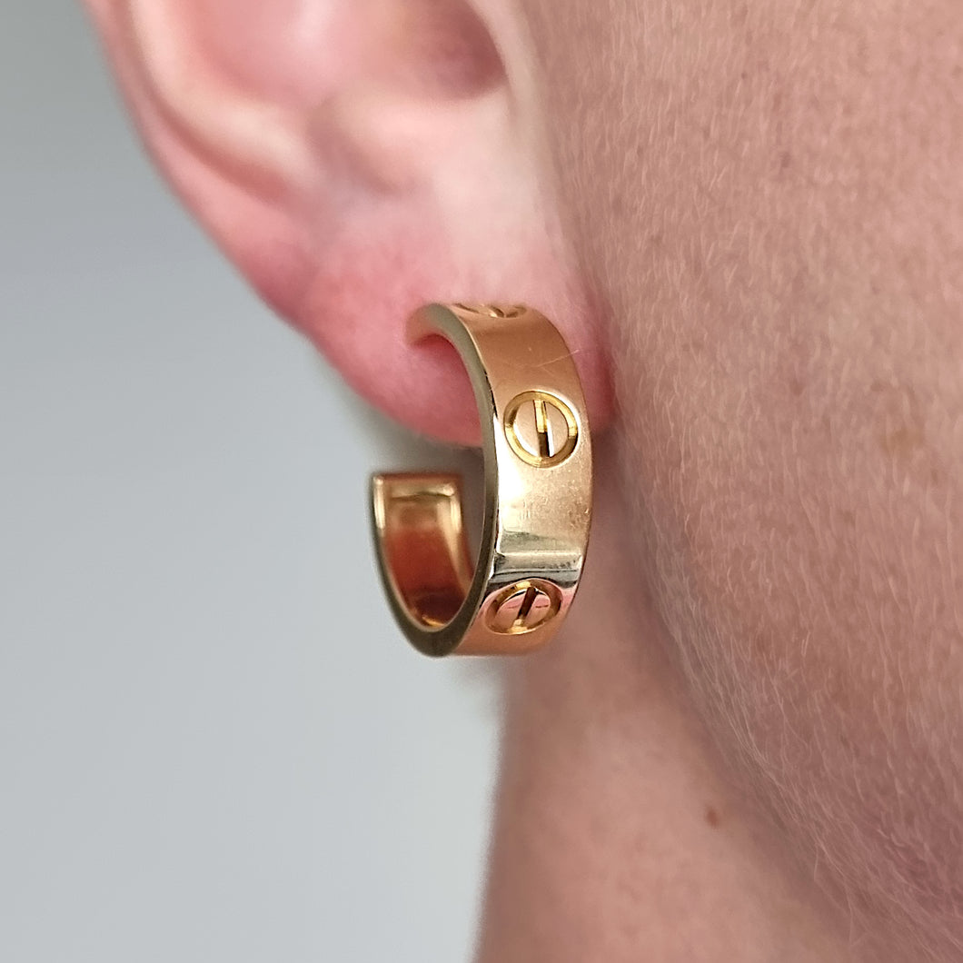 Gold Cartier hoop earring worn on an ear with a neutral background